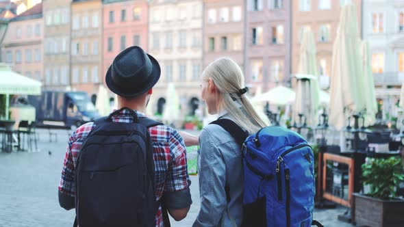 Back View of Tourists Couple with Bags Checking Map on Central City Square