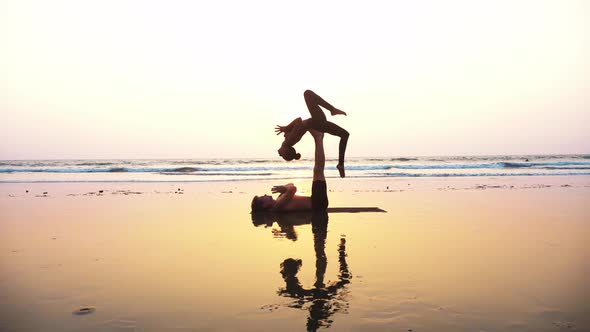 Fit Sporty Couple Practicing Acro Yoga with Partner Together on the Sandy Beach