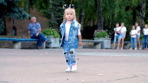 a Little Girl in a Stylish Denim Suit and Ponytails on Her Head Walks Through the Park.