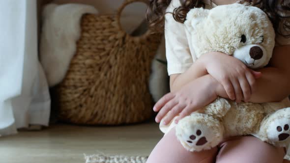 A little girl plays with soft toys sitting on the bed.