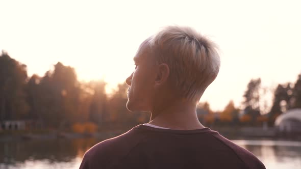 Back View of a Man Standing on the Rocky Pier Enjoying Sunset Over Lake