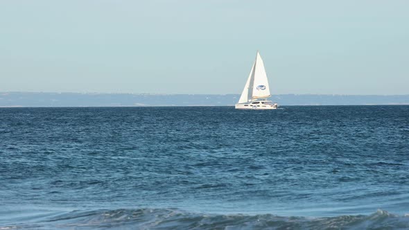 catamaran Boat Heading Out To Sea with some waves crashing onto beach, Cascais