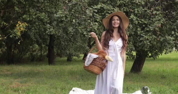 Young Beautiful Woman Walks Through the Garden with a Basket in Her Hands and Smiles