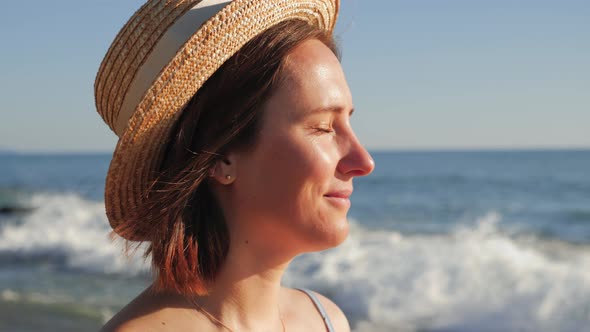 Portrait of young girl in straw hat standing on beach with closed eyes