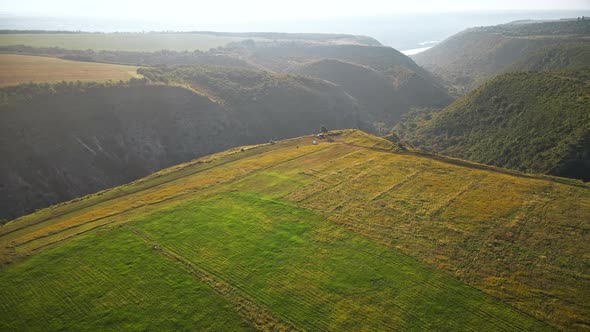 Aerial drone view of a valley with hill slopes covered with lush greenery, fields, water in the dist