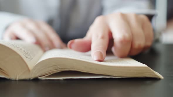 Close-up of a book on which woman's hand moves her finger reading. Woman reads a book