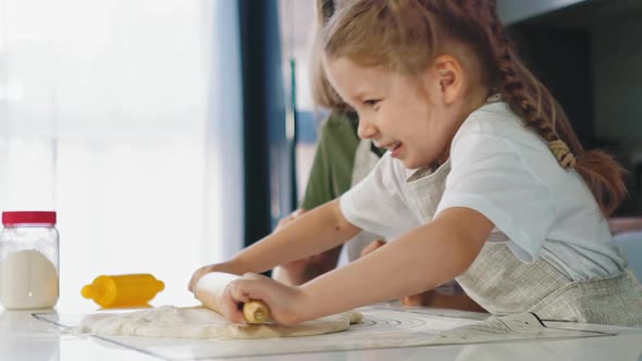 Girl in Apron Rolls Dough Cooking with Mother at Table