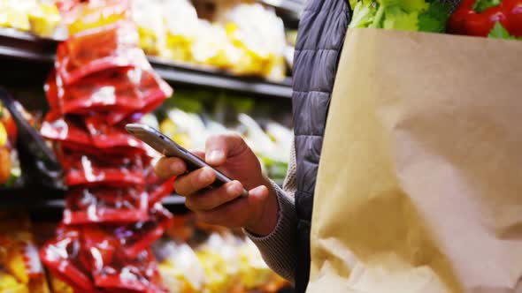 Man using mobile phone while holding grocery bag