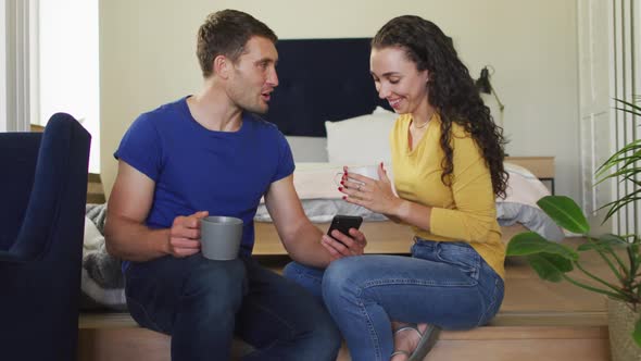 Happy caucasian couple drinking coffee and using smartphone