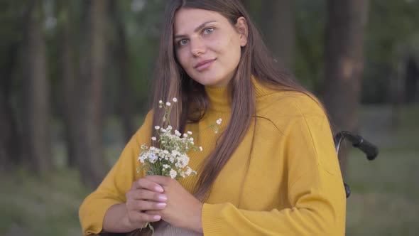 Portrait of Positive Beautiful Caucasian Woman Sitting on Wheelchair with Bouquet of Wildflowers and