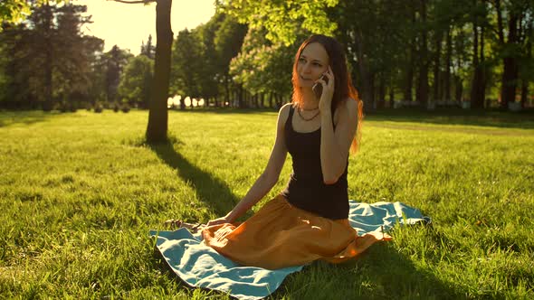 Female Sitting, Talking During a Phone Call Outdoors in the Park