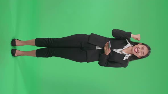 Full Body Of An Asian Business Woman Celebrating While Using Mobile Phone In The Green Screen Studio