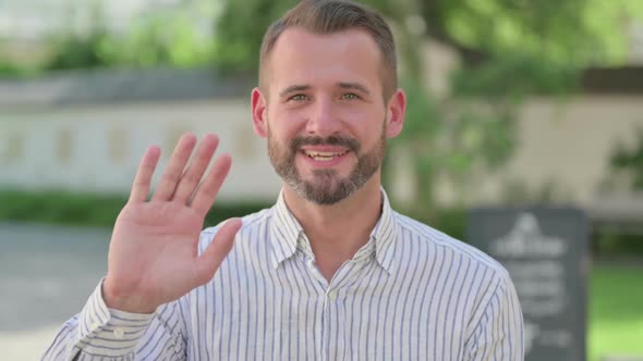 Outdoor Portrait of Middle Aged Man Waving at Camera Welcoming