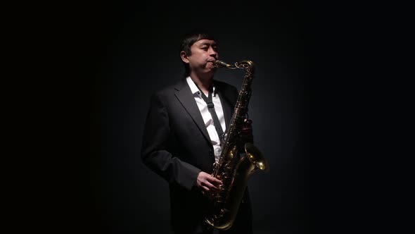 Male saxophonist performs alone with a saxophone playing in studio on a black background.