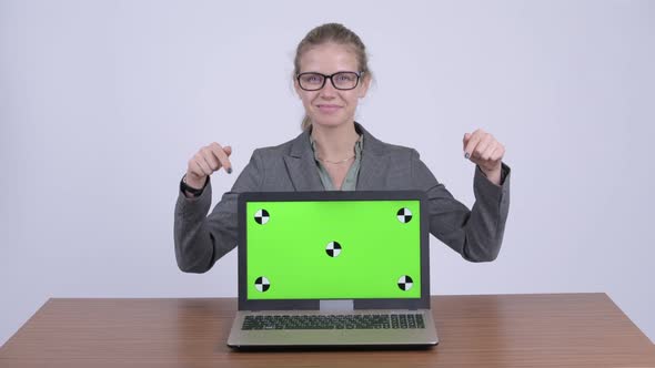 Young Happy Blonde Businesswoman Showing Laptop and Giving Thumbs Up at Desk