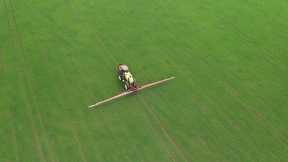 Aerial View of Farming Tractor Plowing and Spraying Green Wheat Field