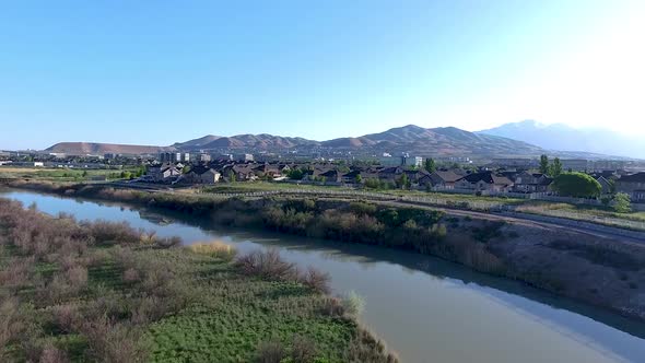 Low aerial approach over a river to towards an urban suburb with mountains in the background