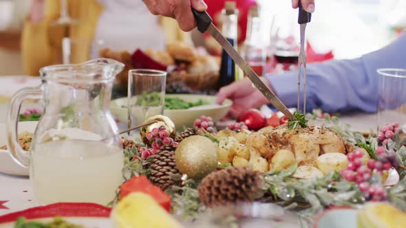 Mid section of person holding fork and knife cutting chicken into pieces during christmas at home