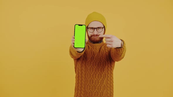 Funny Hipster Caucasian Bearded Guy in a Yellow Beanie and an Orange Sweater Pointing to His Mockup