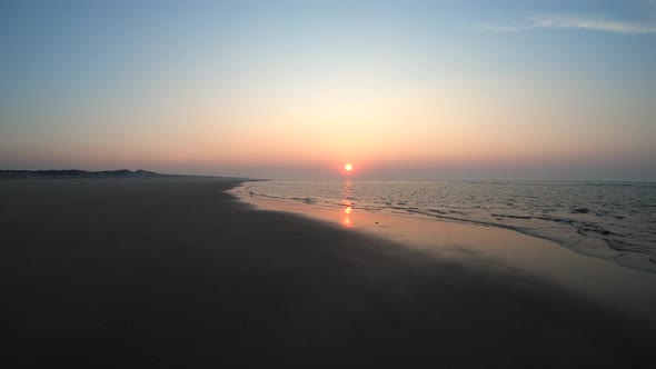 Aerial, drone shot low, waves at a beach, sunset in the background, on Langeoog island