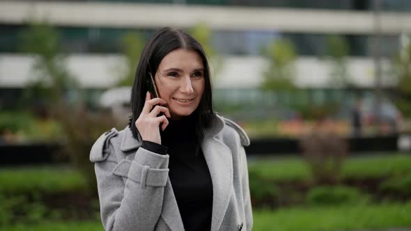 Portrait of a Brunette in a Gray Coat Against a Background of Blurred Modern Buildings