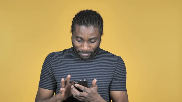Casual African Man Excited for Success While Using Smartphone Isolated on Yellow Background