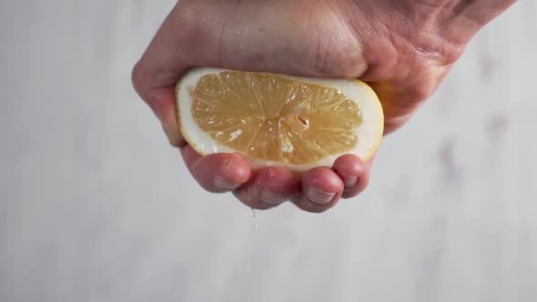 A male hand squeezes half a ripe lemon with seeds 