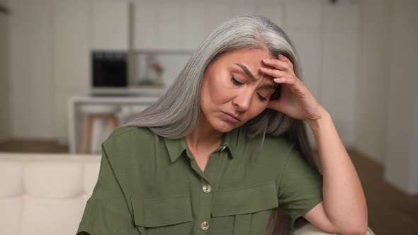 Tired Grayhaired Mature Woman Sitting on the Sofa at Home Rubbing Temple with Suffering Face