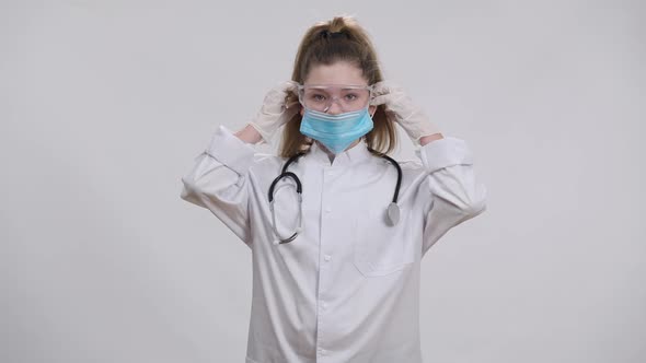 Little Caucasian Nurse Doctor Putting on Medical Covid19 Face Mask Looking at Camera