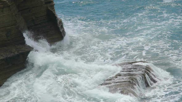 Sea Waves Breaking Into Splashes Against Rocky Cliff Creating Foam by Coastline