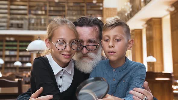 Schoolgirl and Schoolboy Sitting on Grandfather's Knees and Listening How He Reading Book