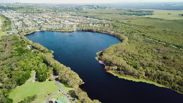 Aerial footage showing tea-tree coloured freshwater coastal lake, houses in background. Location Lak