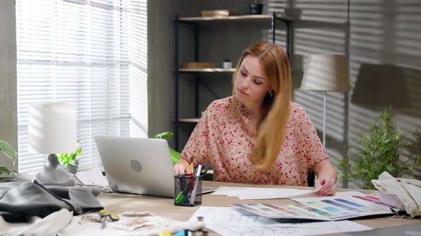 Female Fashion Designer Look at Laptop Working with Sketches in Studio Atelier