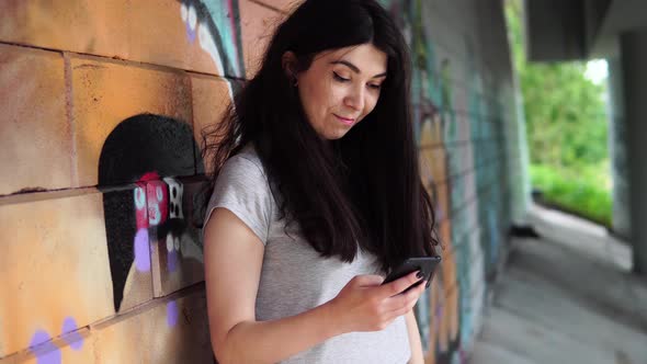 Street Portrait of a Woman in Everyday Clothes. The Female Uses the Phone. Woman Dials a Message on