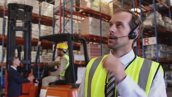 Male warehouse manager talking with headset in loading bay 4k