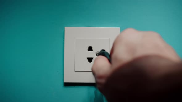 Man Inserts Plug Into Electrical Socket On A Blue Wall