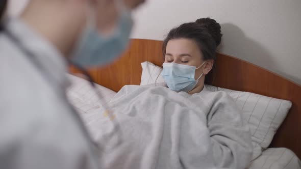 Portrait of Young Woman Lying in Bed in Hospital Ward Talking to Doctor Complaining Symptoms