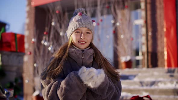 Cute Happy Girl Holding Snow on Palms and Blowing at Camera