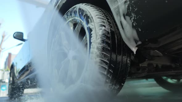 Closeup Washing Off White Foam From Car Wheel with Water