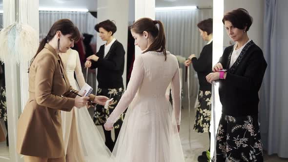 Two Female Dress Designers and a Beautiful Bride Trying Her Wedding Gown in Elegant Boutique or