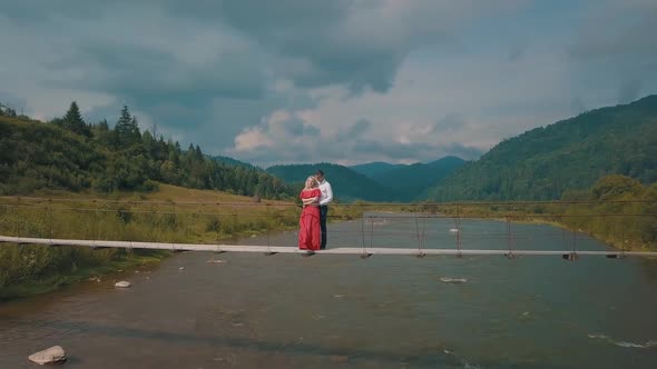 Couple Stands on Bridge Over a Mountain River. Love of Man and a Woman