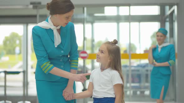 Charming Cheerful Woman in Stewardess Uniform Talking To Cute Little Caucasian Girl in Airport