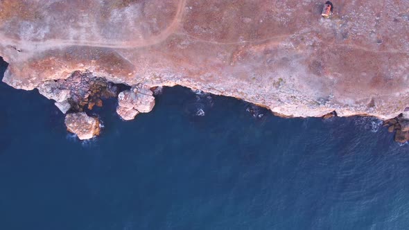 Top down aerial view of waves splash against rocky seashore, background. Flight over high cliffs of