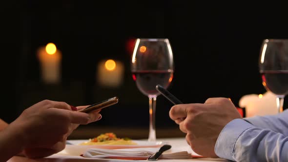 Couple Sitting in Restaurant Scrolling Smartphones, Ignoring Real Communication