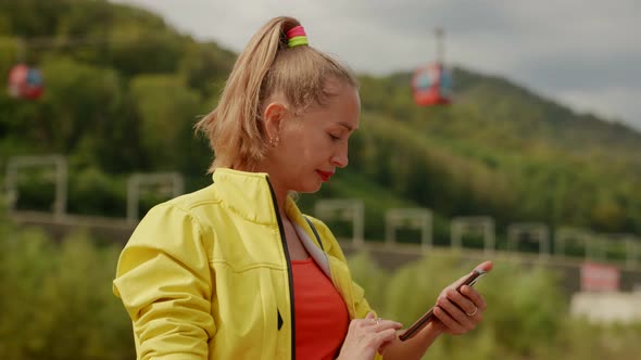 Portrait of a Blonde in Red and Yellow Clothes with a Phone in Hands Against the Background of