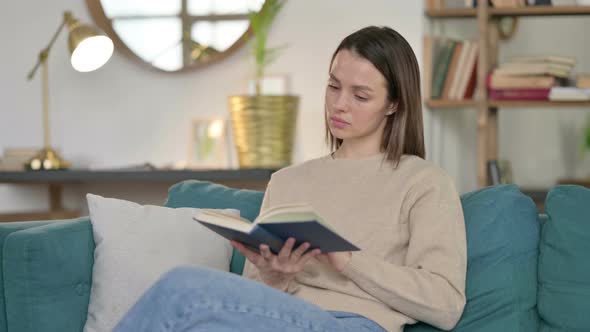 Young Woman Sitting Reading Book on Sofa 