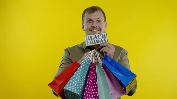 Surprised Man Showing Shopping Bags and Black Friday Inscription in His Mouth. Yellow Background