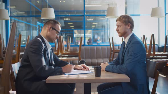 Small Business Owner Signing Mortgage Contract with Bank Agent in Closed Cafe