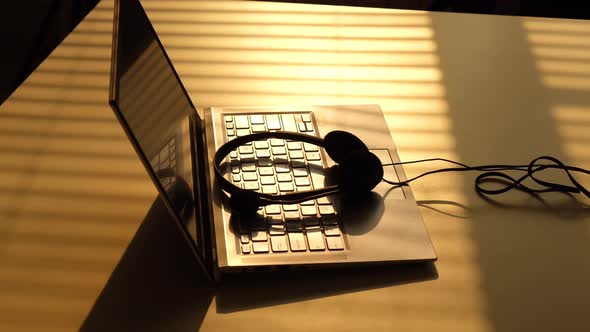 A Man Takes Headphones From the Keyboard of a Laptop in the Sunbeams of the Sunset