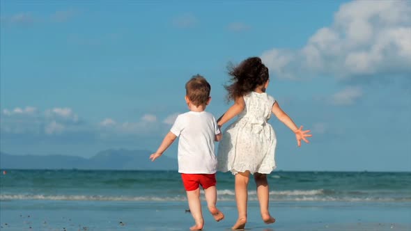 Lovely Children, Girl and a Boy Holding Hands Each Other Running Along the Tropical Coast